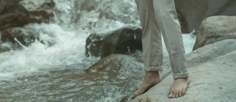 man wearing trousers slightly rolled up by waterfall 